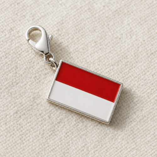 A rectangular charm featuring the red and white horizontal stripes of the Indonesian flag, attached to a silver lobster clasp, displayed on a textured beige fabric background.